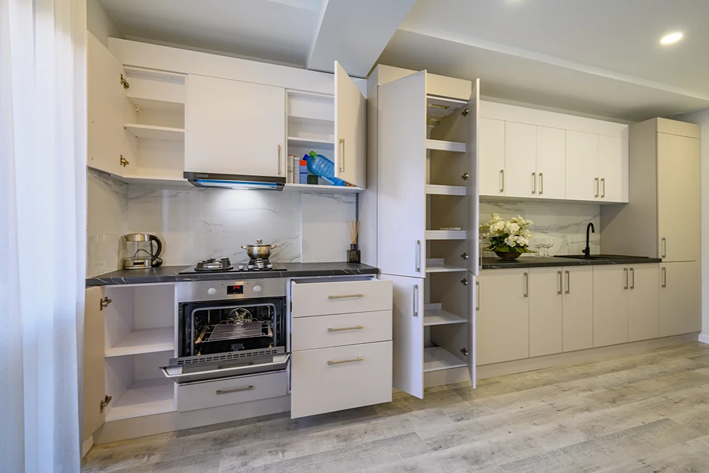 Beyaz dolaplı modern mutfakta açık dolap kapakları ve fırın görülüyor