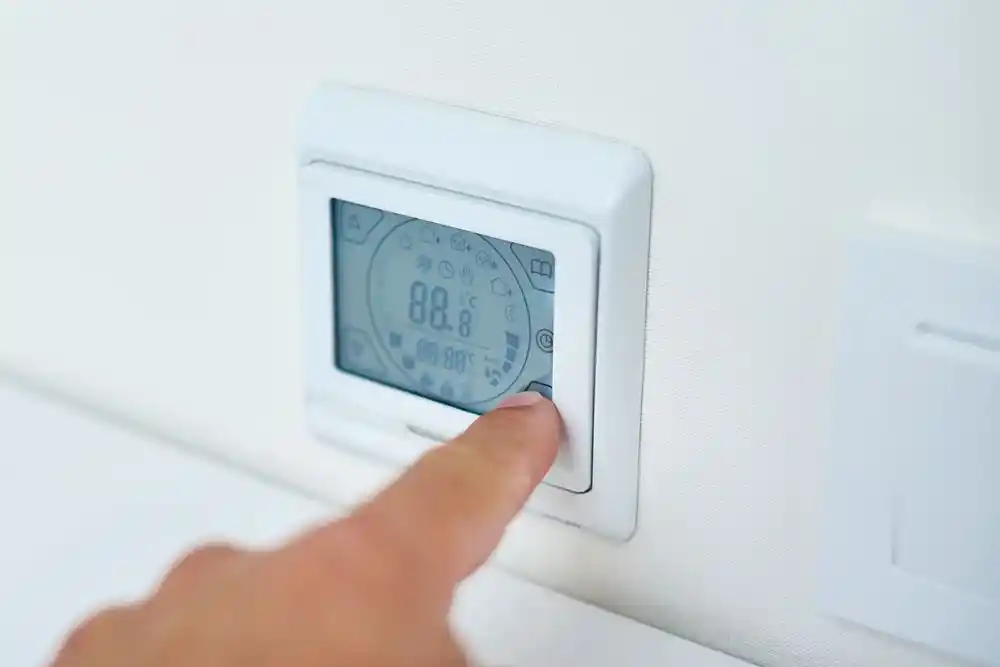 Bir parmak duvara monte dijital termostatın düğmesine basıyor