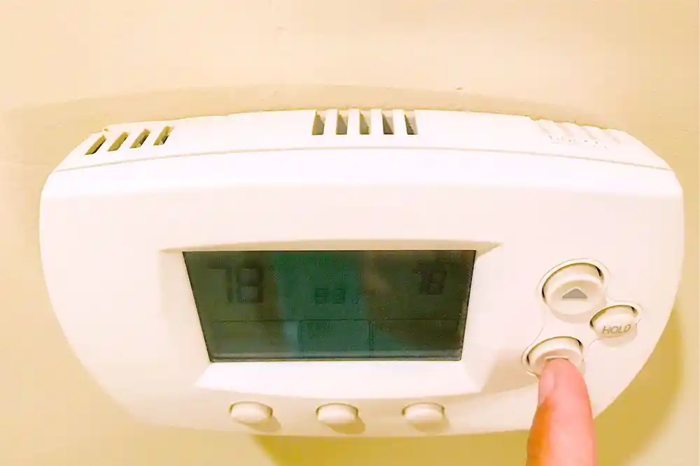 Duvara monte dijital termostatın düğmesine basan parmak