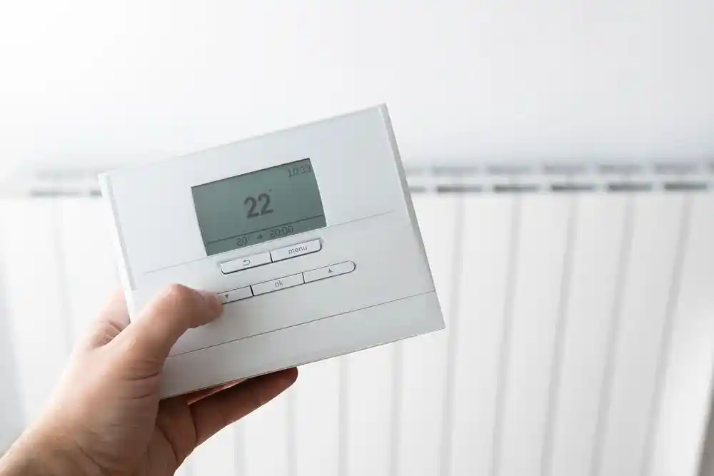 Bir el, ekranda 22° gösteren dijital termostat kumandasını tutuyor