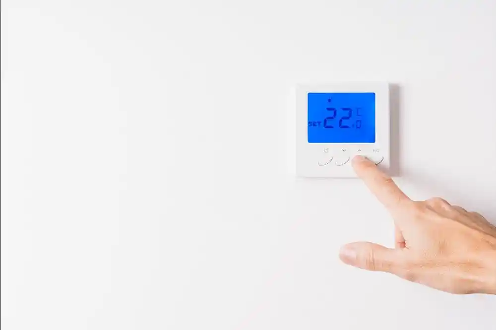 Bir el, duvara monte dijital termostatı ayarlıyor; ekranda 22 °C gösteriliyor