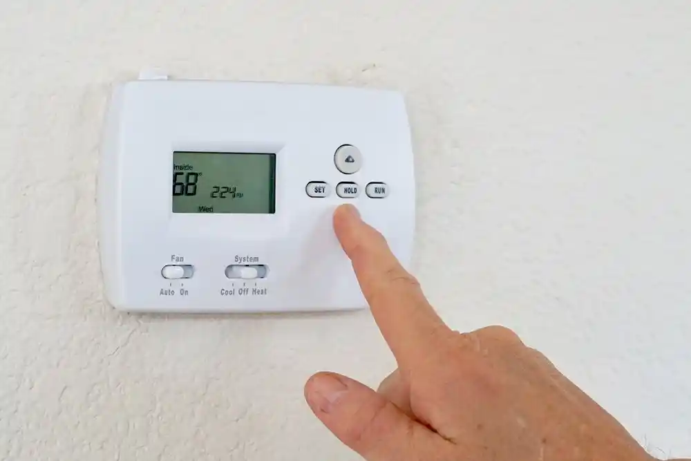 Bir parmak, duvara monte termostatın HOLD düğmesine basıyor