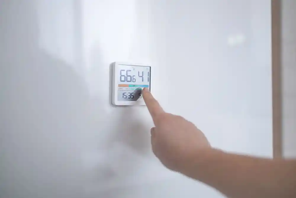 Bir kişi duvardaki dijital termostatın düğmesine basıyor