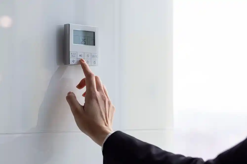 Bir kişi duvara monte dijital termostatın düğmesine basıyor