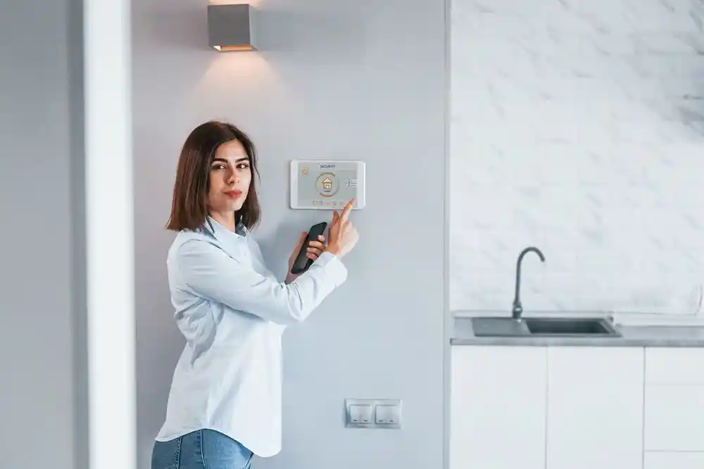 Kadın, elindeki akıllı telefonla duvardaki güvenlik paneline dokunuyor