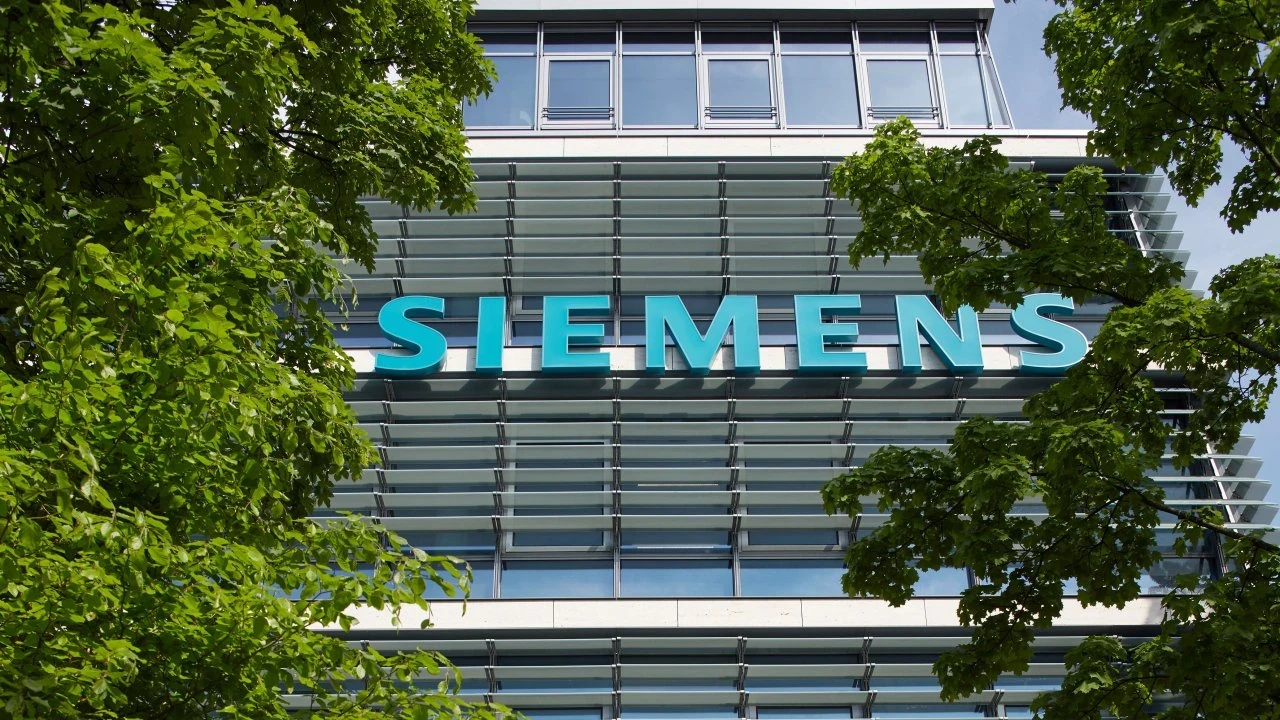 Ağaçların arasından görülen modern bir binanın cephesinde büyük Siemens logosu
